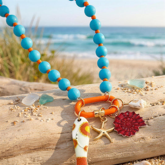 Turquoise beaded charm-holder necklace with fish and spiral shell charms on driftwood