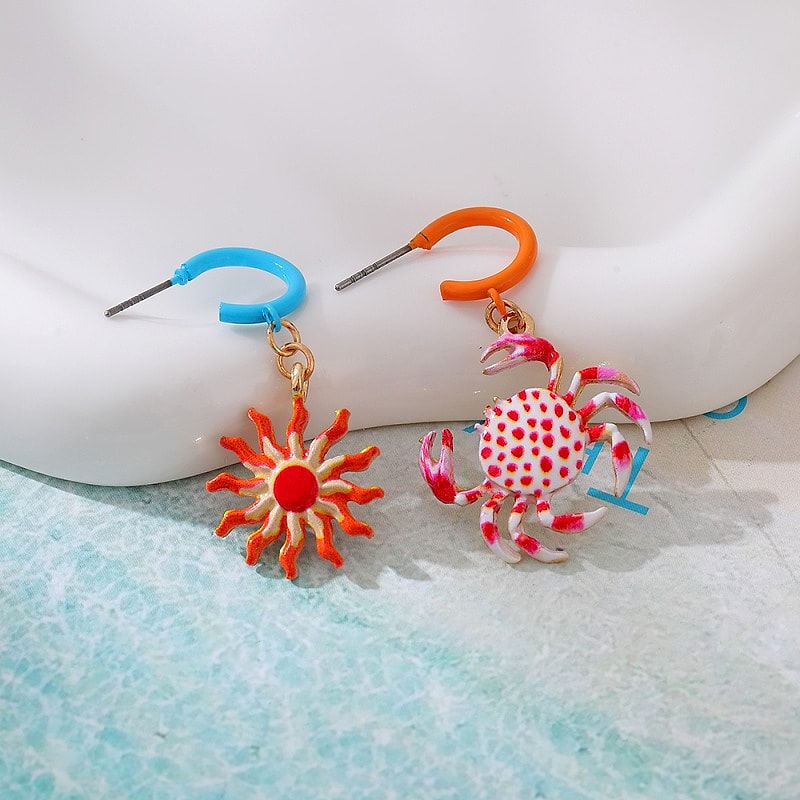 Asymmetric enamel crab and sun dangle earrings on white fabric