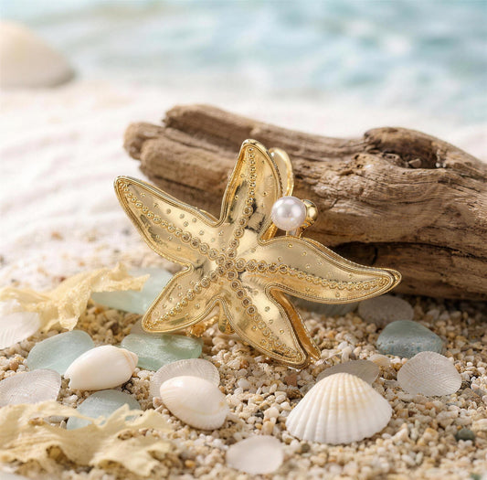 Gold starfish hair claw with pearl on driftwood and sand